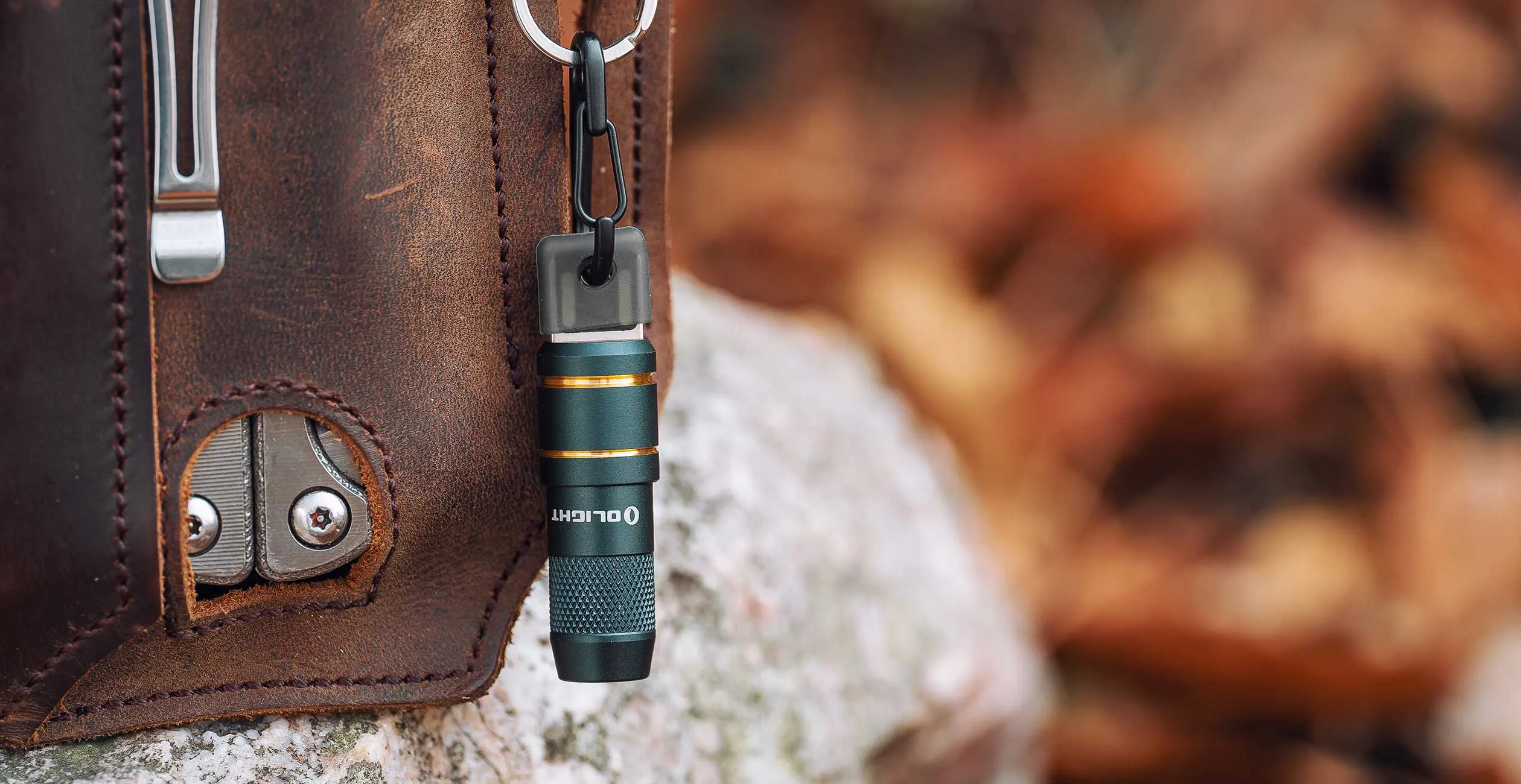 Mitternachtsblaue Olight iMini 2 an einem Karabiner neben einer Ledertasche