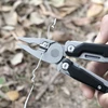 Multitool-Zange schneidet Metalldraht im Freien vor verschwommenem Hintergrund aus Laub