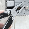 Multitool-Zange löst rostige Sechskantschraube an grauer Kunststoffbox