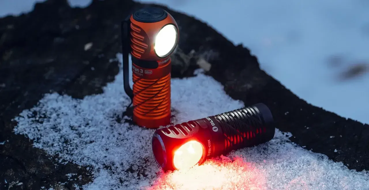 Zwei Taschenlampen im Schnee: orange mit weißem Licht, schwarz mit rotem Licht.