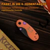 Kizer kompaktes Taschenmesser im Halloween-Design mit orangefarbenem Griff und Kürbis-Motiv auf Holzgrund.