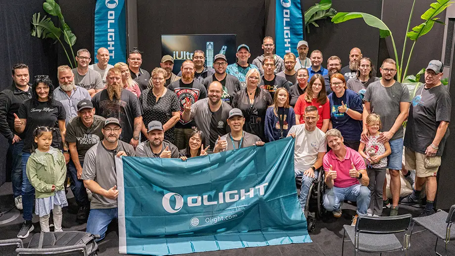 Olight-Community: Diverse Gruppe Menschen posiert glücklich mit Olight-Banner auf Veranstaltung.