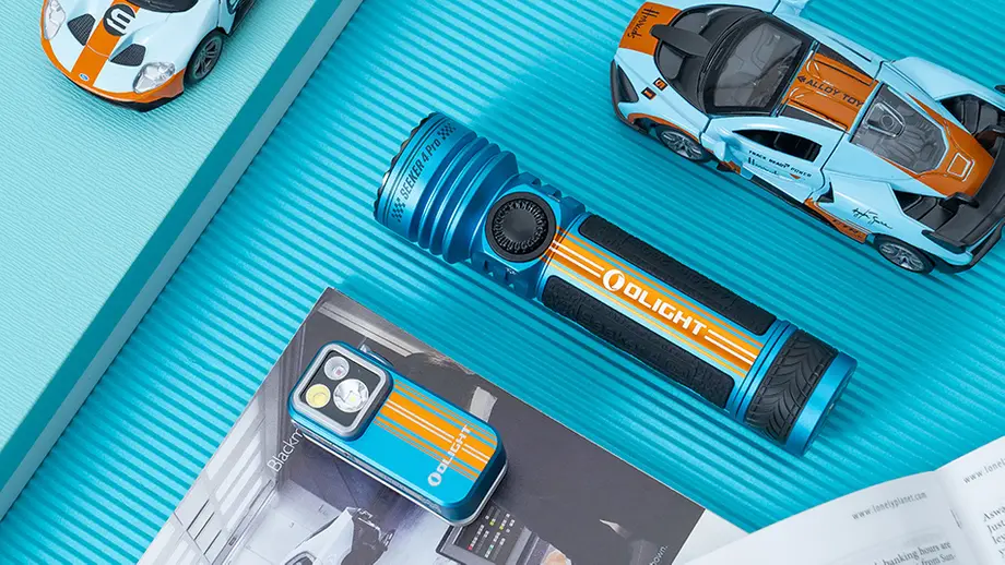 Olight Seeker 4 Pro und kleine Olight Taschenlampe in Blau-Orange mit Rennwagen-Design, umgeben von Modellautos.