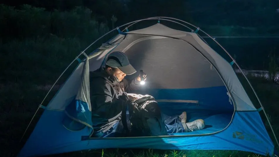 Camper im Zelt beleuchtet nachts Rucksack mit Taschenlampe.