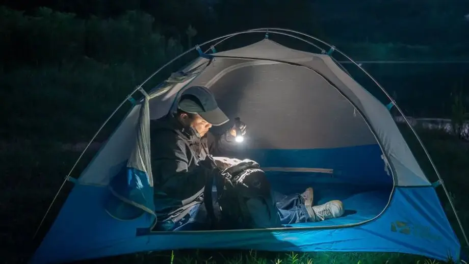 Camper im Zelt beleuchtet nachts Rucksack mit Taschenlampe.