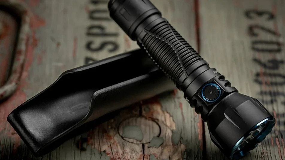 Schwarze taktische LED-Taschenlampe mit blauem Ring und Holster auf Holz.