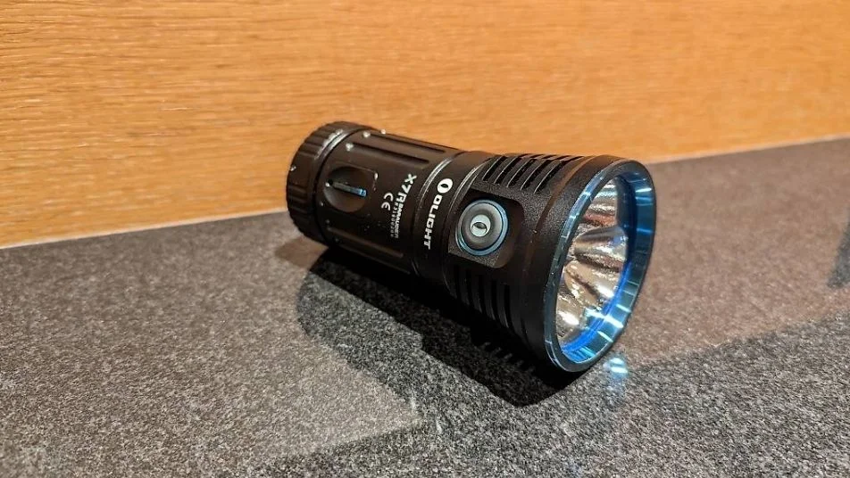 Schwarze Olight X7R Marauder LED-Taschenlampe mit blauem Akzentring auf grauem Untergrund.