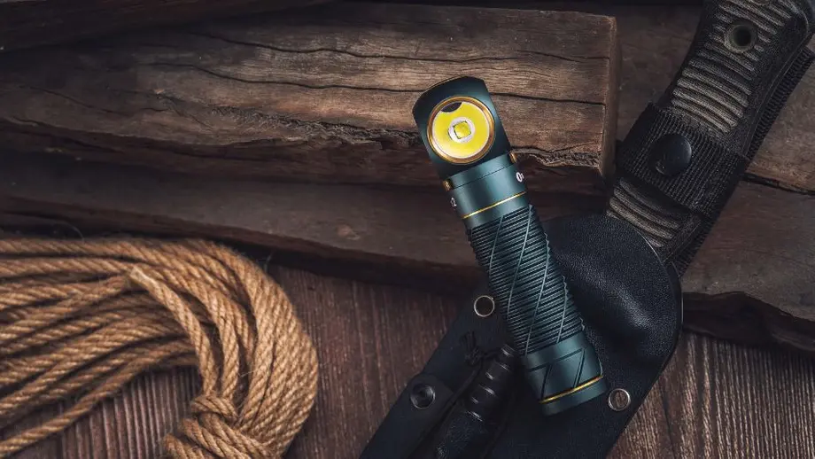 Grüne Winkeltaschenlampe mit gelb leuchtender LED, Messer und Seil auf dunklem Holzgrund. Outdoor-Ausrüstung.