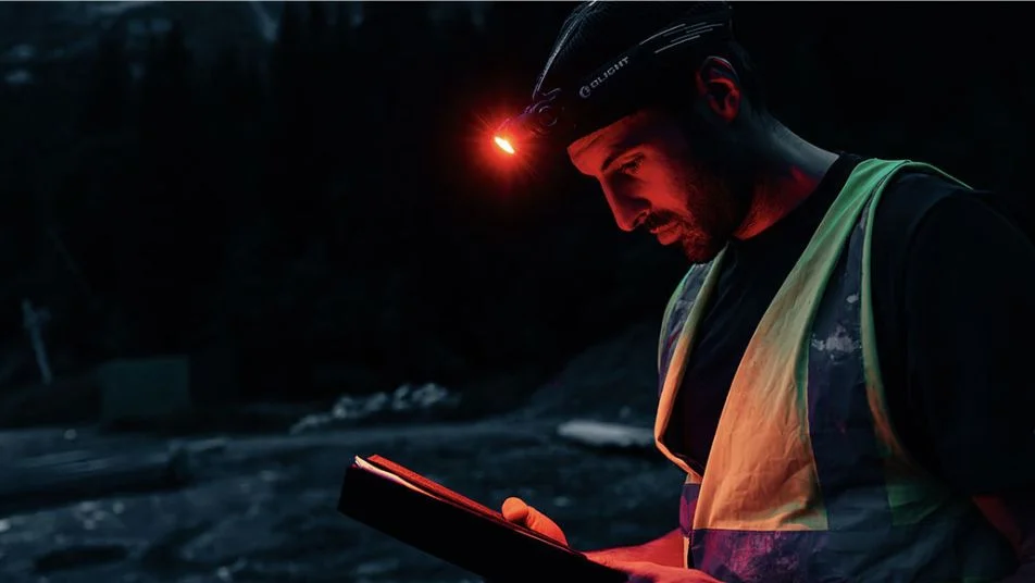 Mann mit Olight Stirnlampe (Rotlicht) und Warnweste bei Nachtarbeit.