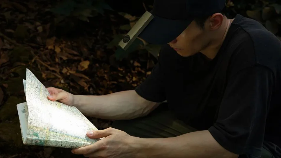 Person mit Stirnlampe studiert Faltkarte im dunklen Wald, sucht den Weg.