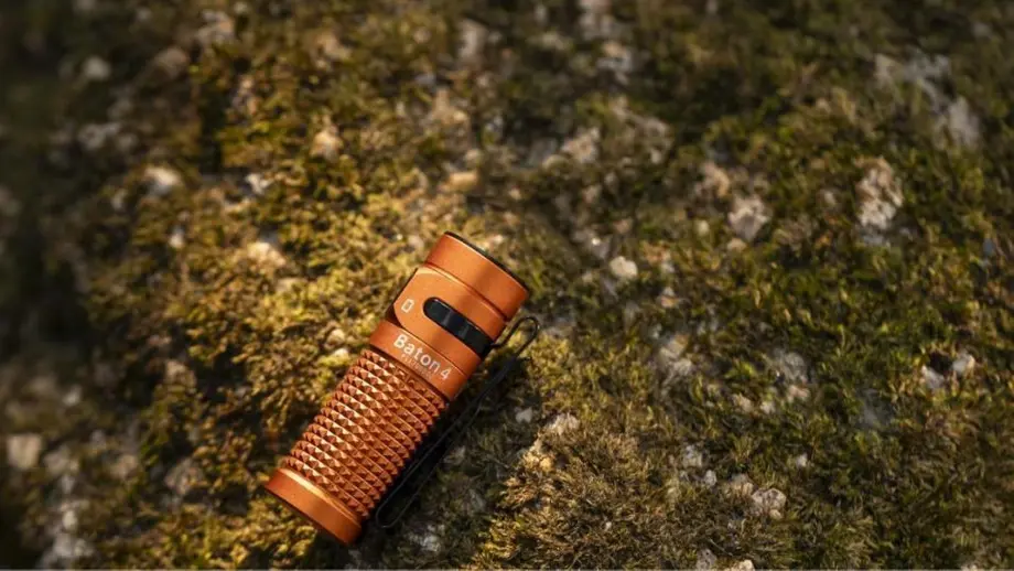 Orangefarbene Olight Baton 4 Taschenlampe auf moosbewachsenem Untergrund.
