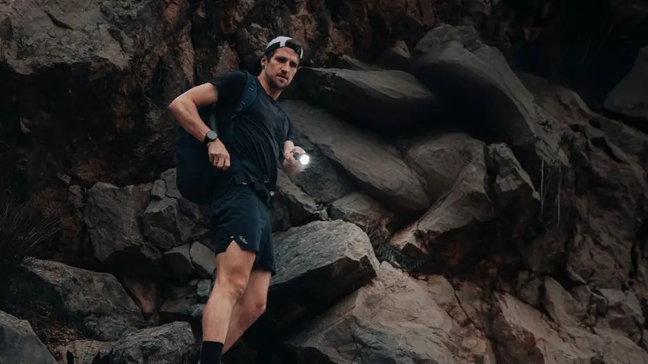 Mann mit Rucksack und leuchtender Taschenlampe erkundet Felsgelände bei Nacht.