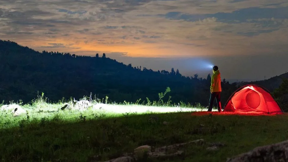 Abenteuerliches Nachtcamping mit Stirnlampe und rotem Zelt in den Bergen