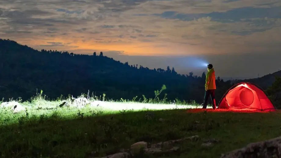 Abenteuerliches Nachtcamping mit Stirnlampe und rotem Zelt in den Bergen