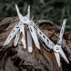 NexTool Multitool mit Zange, Säge und Messer ausgeklappt auf einem Holzstamm für Outdoor und Camping