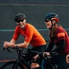 Zwei lachende Radfahrer mit Helmen und Sportkleidung auf Rennrädern bei einer Pause auf der asphaltierten Strecke
