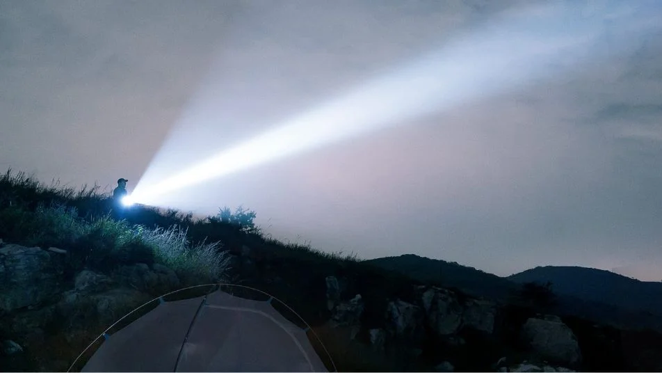 Mann mit starker Taschenlampe leuchtet in dunklen Nachthimmel über Campingzelt auf Berggipfel.
