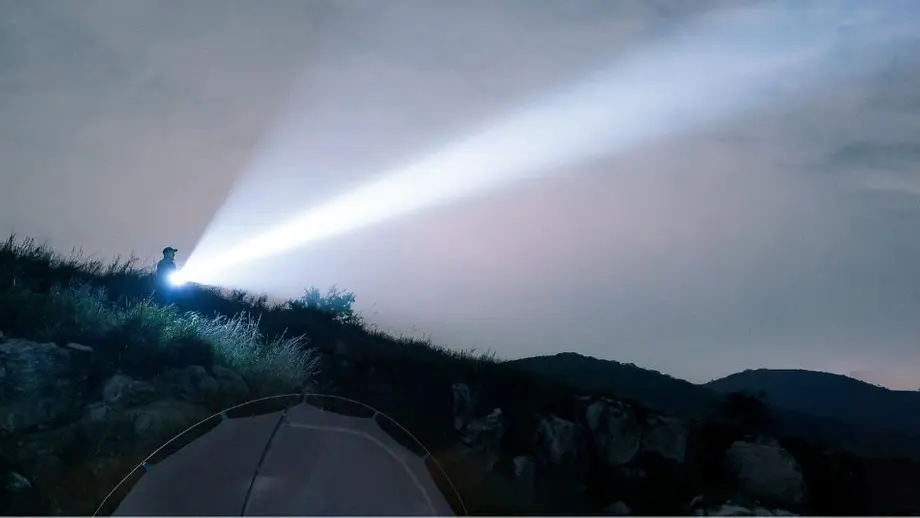 Mann mit starker Taschenlampe leuchtet in dunklen Nachthimmel über Campingzelt auf Berggipfel.