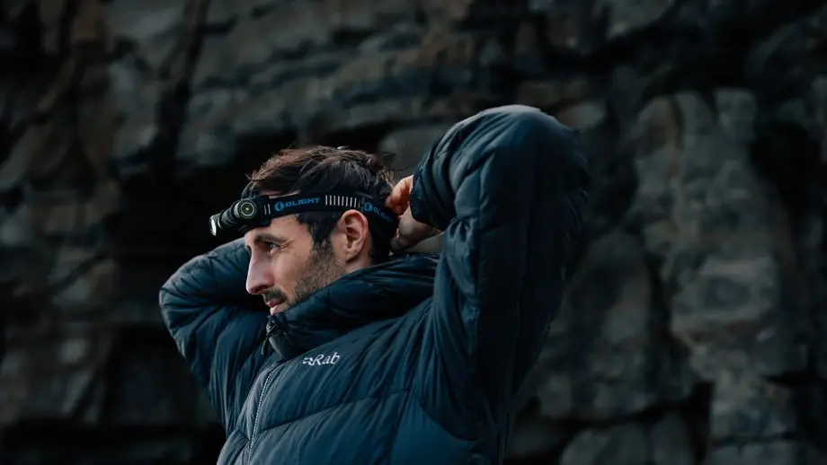 Mann justiert Stirnlampe für Outdoor-Abenteuer in rauer Natur.